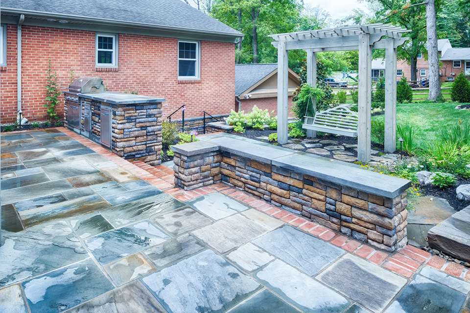 View of a patio with a seat wall and a brick house in the background.